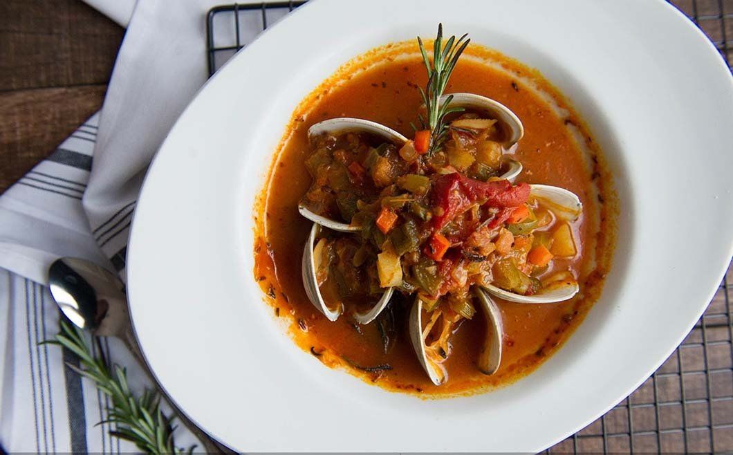 A bowl of soup with clams and vegetables on a table