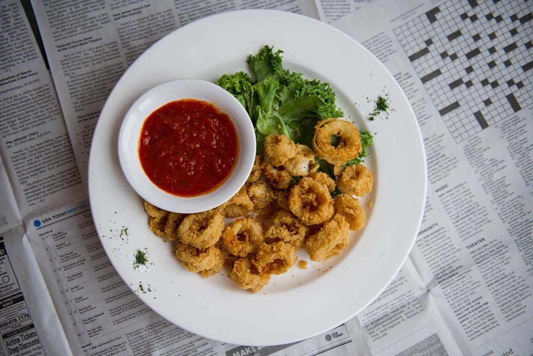 A white plate topped with fried calamari and a small bowl of sauce.
