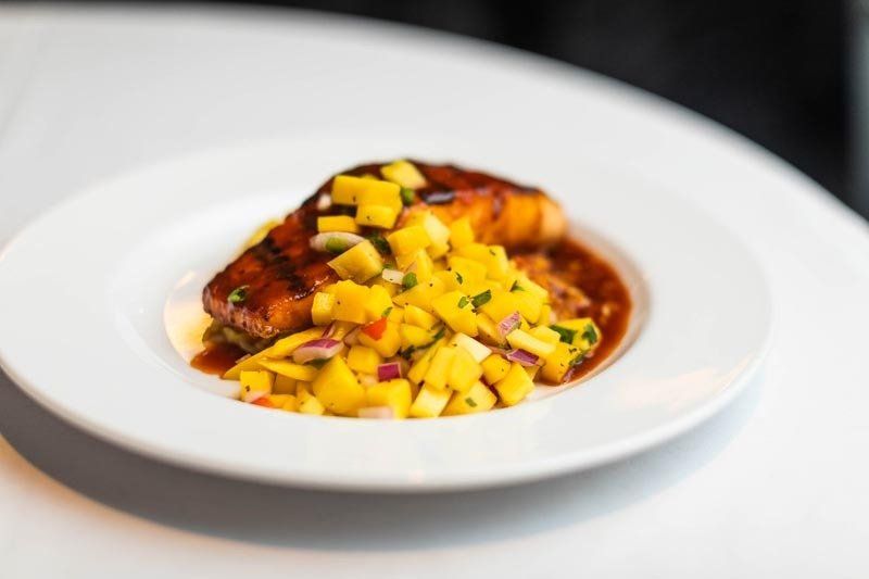 A white plate topped with a piece of meat and mango salsa.