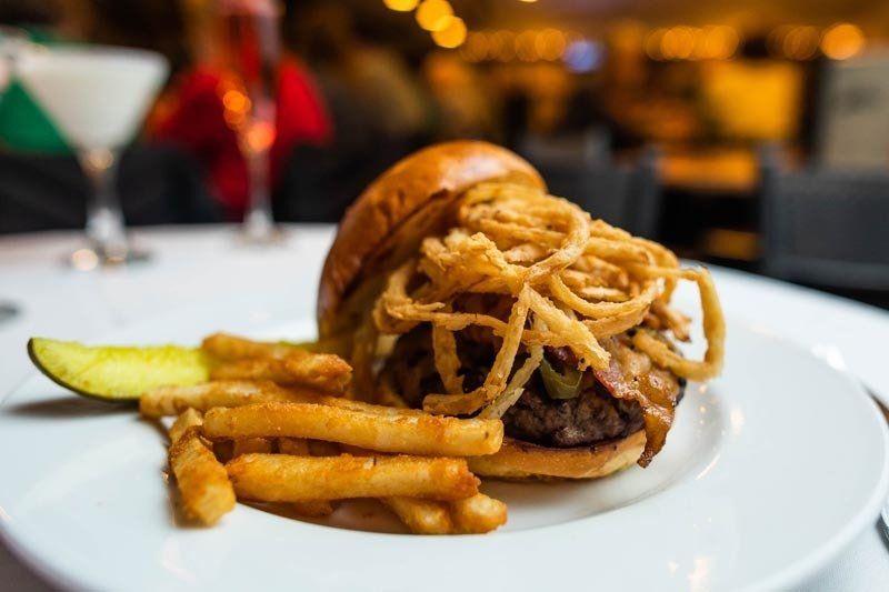 A hamburger with onion rings and french fries on a white plate.