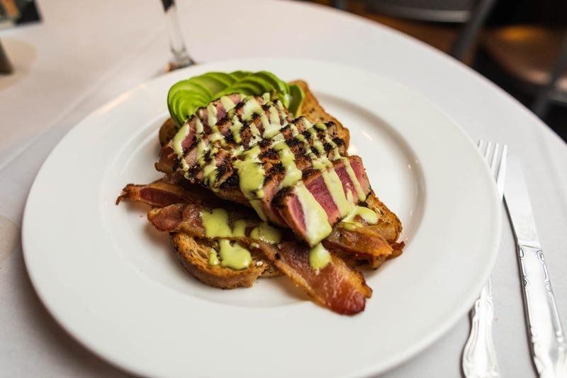 A white plate topped with meat , bacon and avocado on a table.