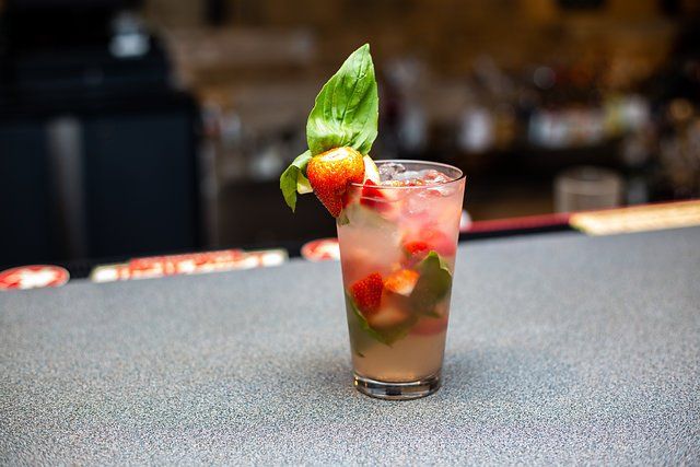A close up of a drink with strawberries and basil on a table.
