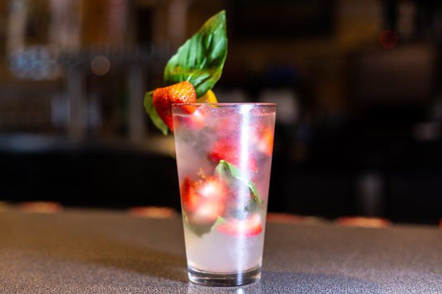 A glass of water with strawberries and basil on a table.