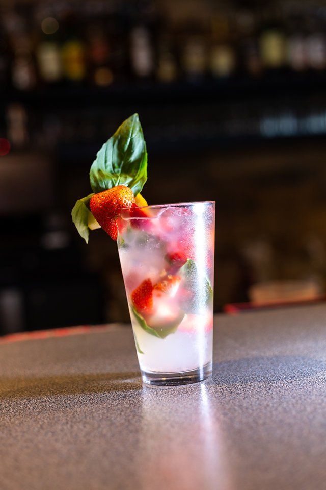 A glass of watermelon juice with strawberries and basil on a bar.