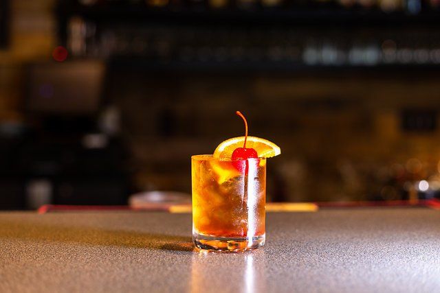 A close up of a cocktail with a cherry and orange slice on a bar.