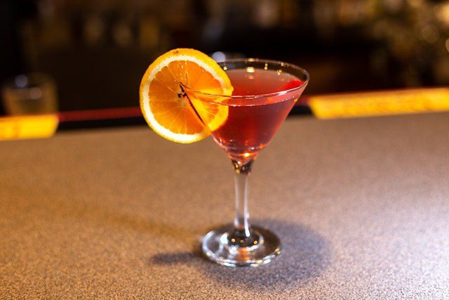 A martini with an orange slice on top of it is on a bar.