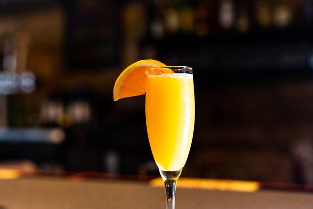 A close up of a glass of orange juice with an orange slice on a bar.