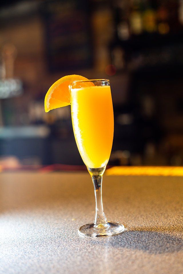 A glass of orange juice with a slice of orange on a bar.