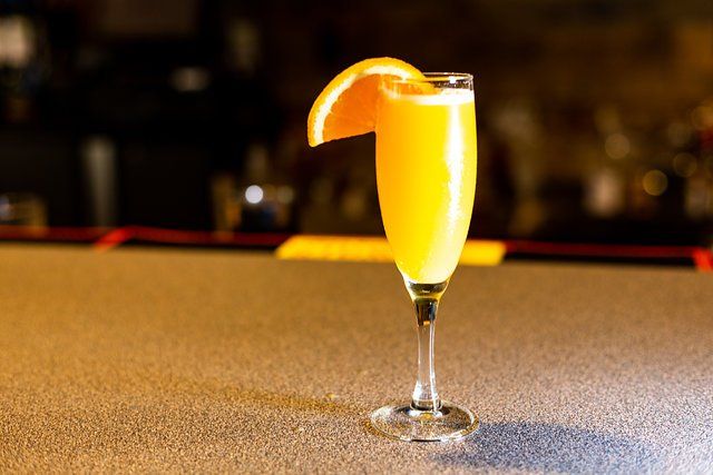 A glass of orange juice with a slice of orange on a bar.