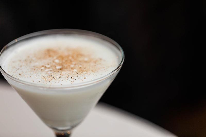 A close up of a white drink in a martini glass on a table.