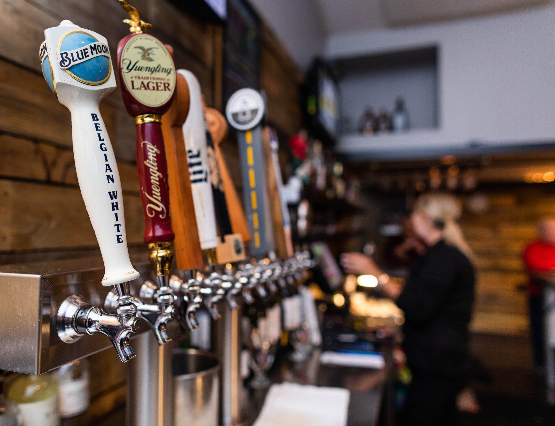A bar with a lot of beer taps and a woman in the background.