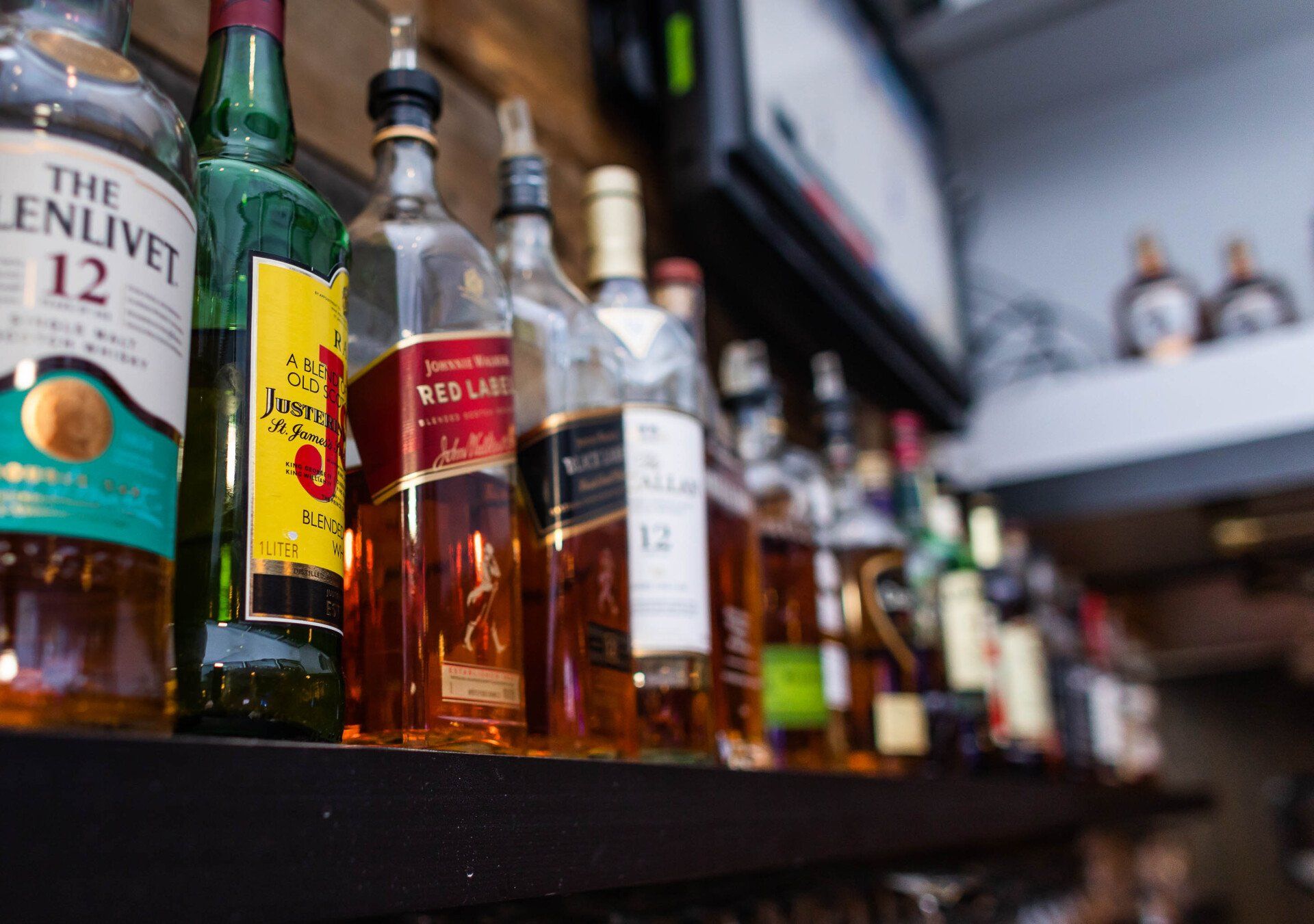 A row of bottles of alcohol are lined up on a shelf.