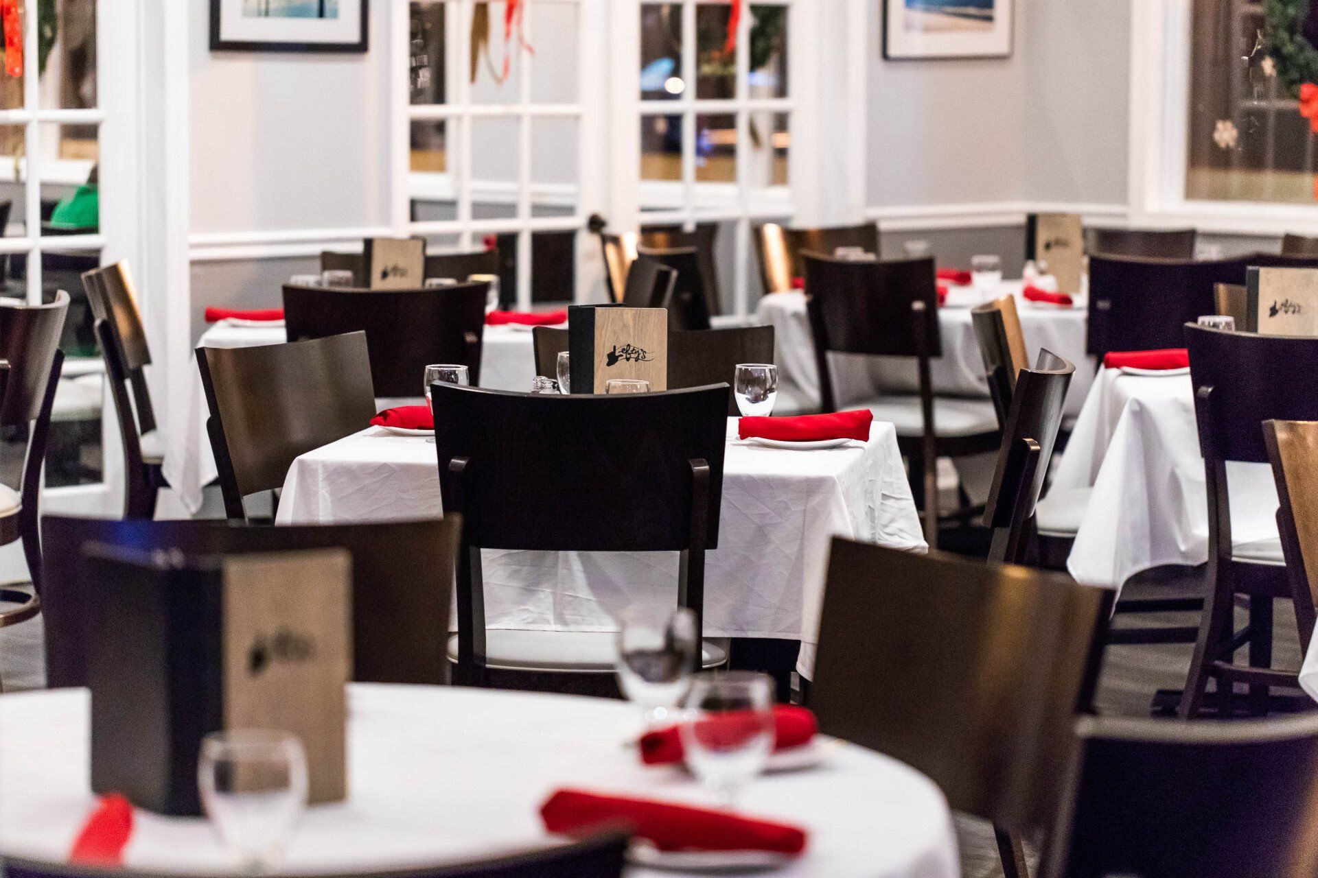 A restaurant filled with tables and chairs with red napkins and wine glasses.