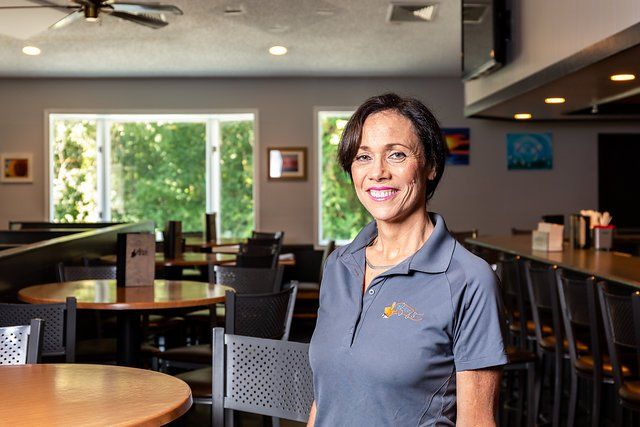 A woman in a gray shirt is standing in a restaurant.