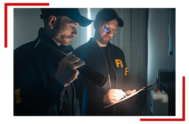 Two men are looking at a clipboard in a dark room.