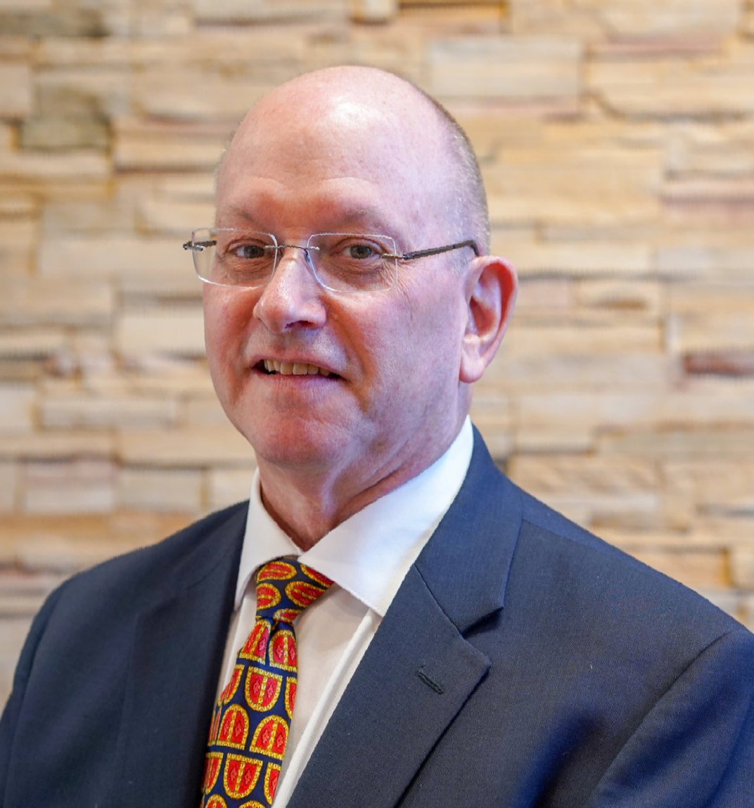 A man in a suit and tie is standing in front of a brick wall