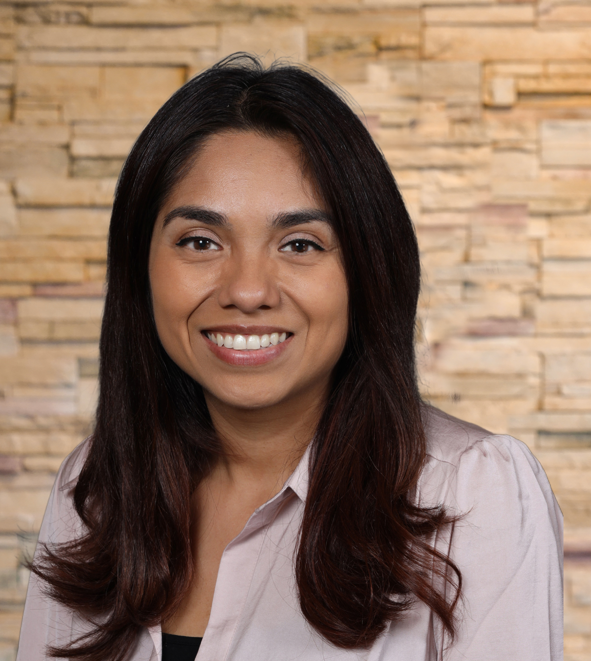 A woman is smiling in front of a brick wall