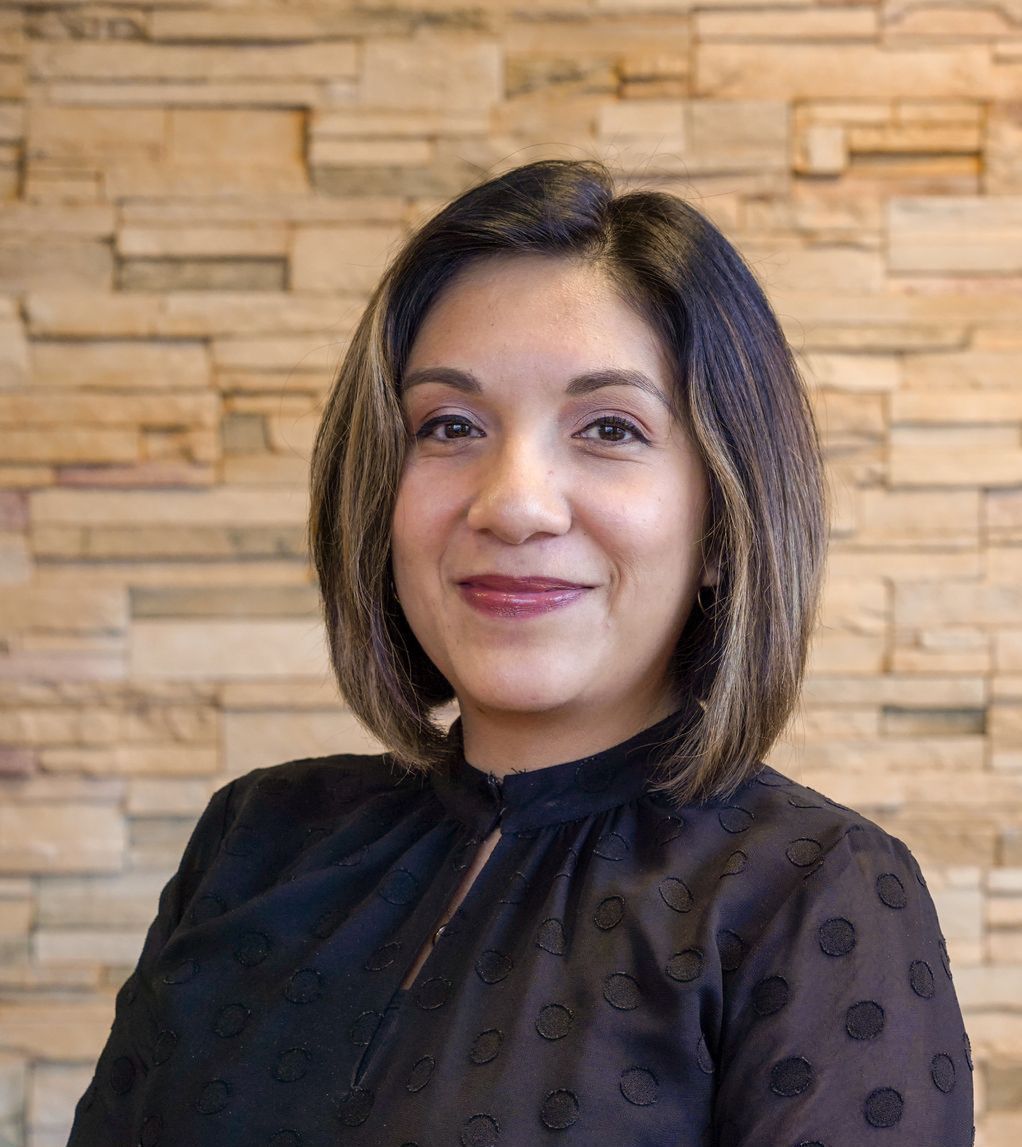 A woman in a black shirt is smiling in front of a brick wall.