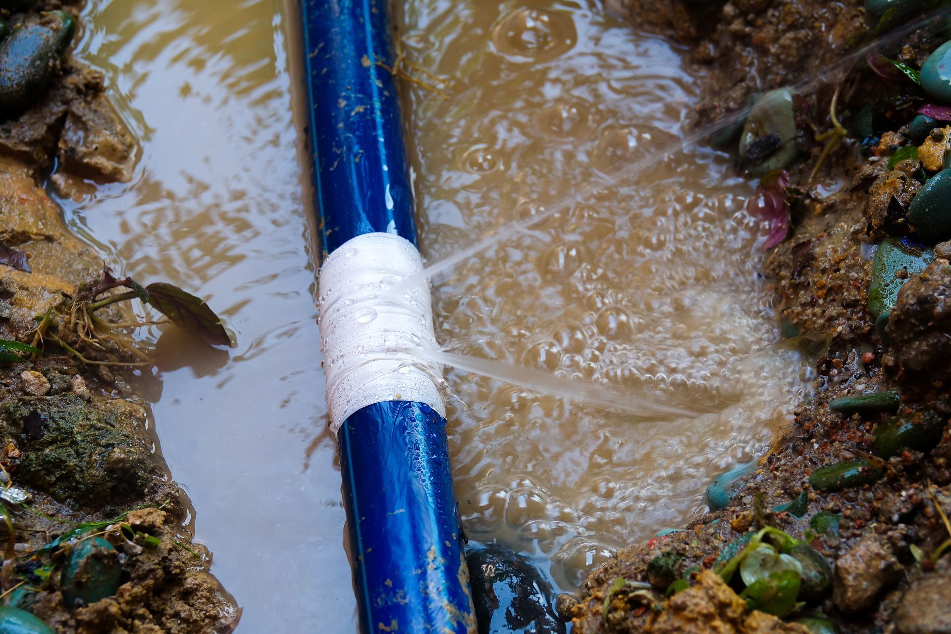Blue pipe in muddy water between rocky banks, with a white band around it