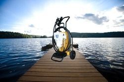 Yellow pressure washer on a wooden dock overlooking a lake with a forest in the background.