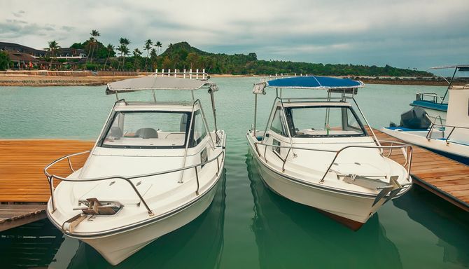 Two white motorboats docked at a pier, blue water, green hills in background.