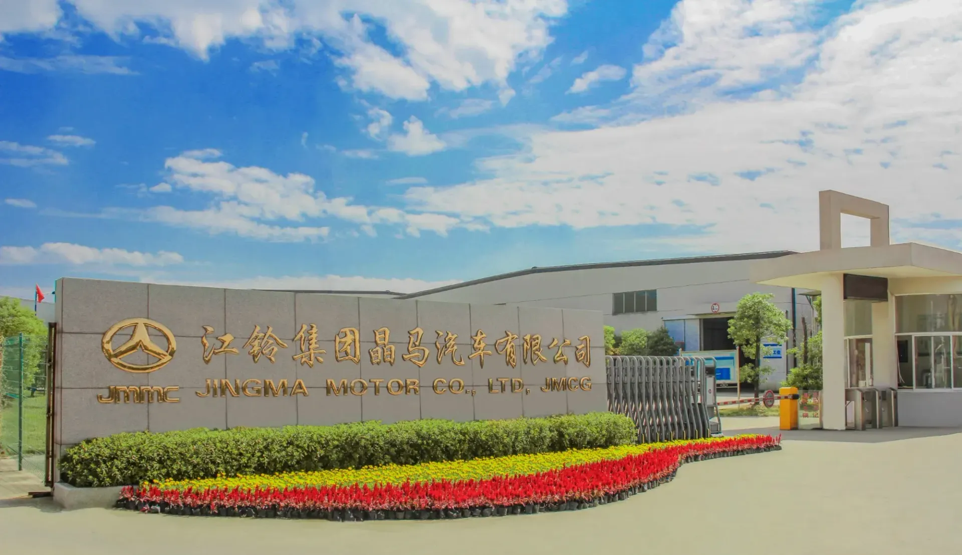 Entrance to a factory with a sign in Chinese and English, under a blue sky with clouds.