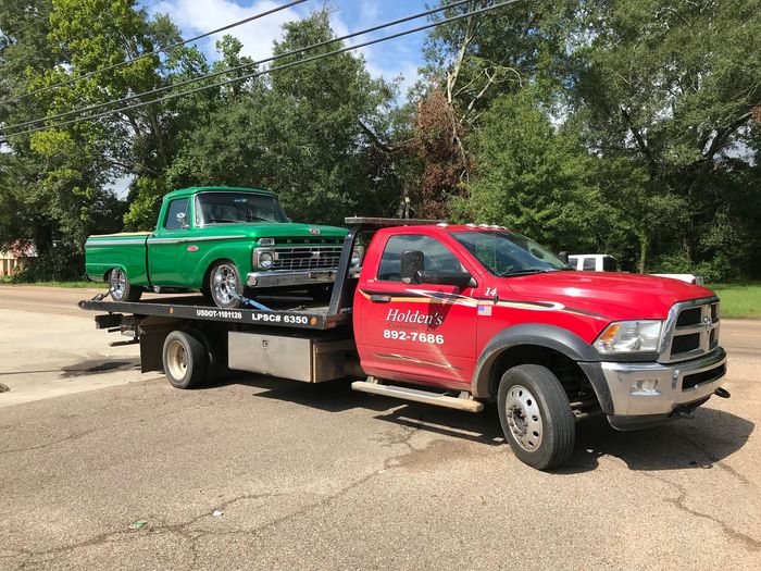 holden's wrecker service flat bed towing an antique truck