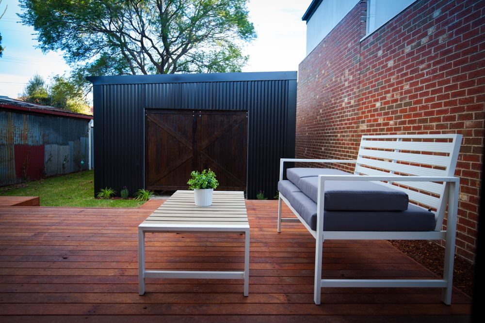 A Wooden Deck With a Couch and a Table in Front of a Brick Wall — Marshall Notaras Hardwoods Pty Ltd In Ballina, NSW