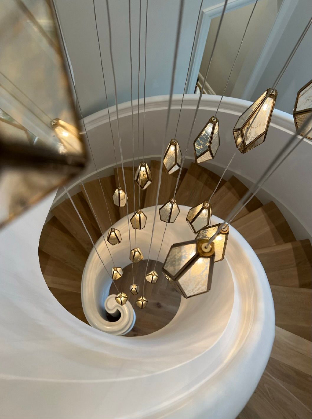 A spiral wooden staircase viewed from above, illuminated by hanging geometric glass pendants.