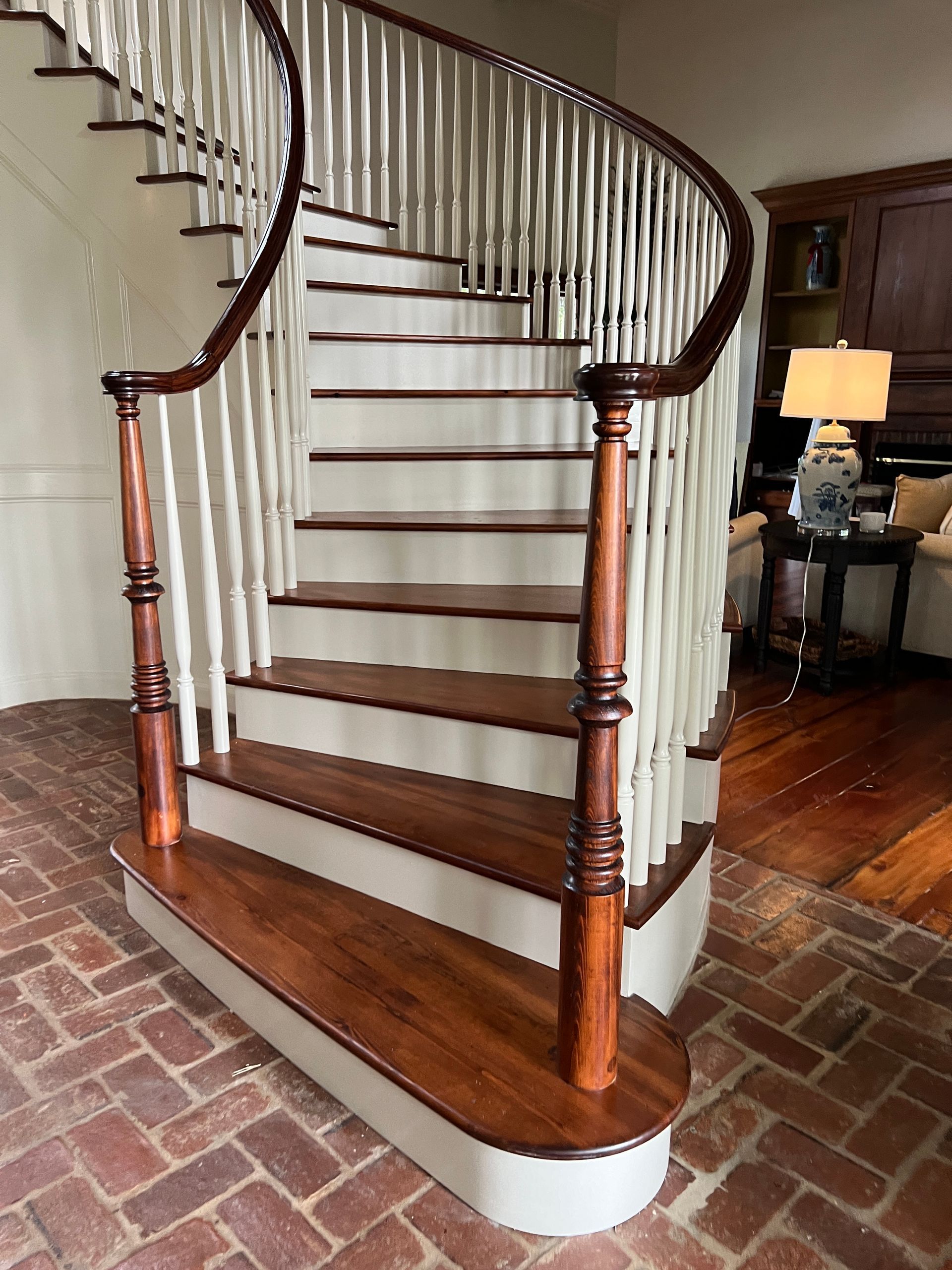Curved staircase with wood treads and white risers, ending with a rounded bottom step on a brick floor.