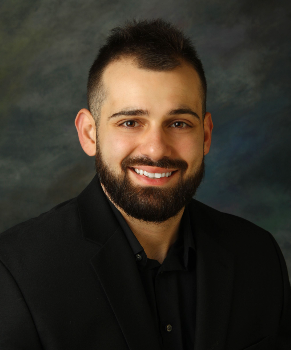A man with a beard is wearing a suit and white shirt.