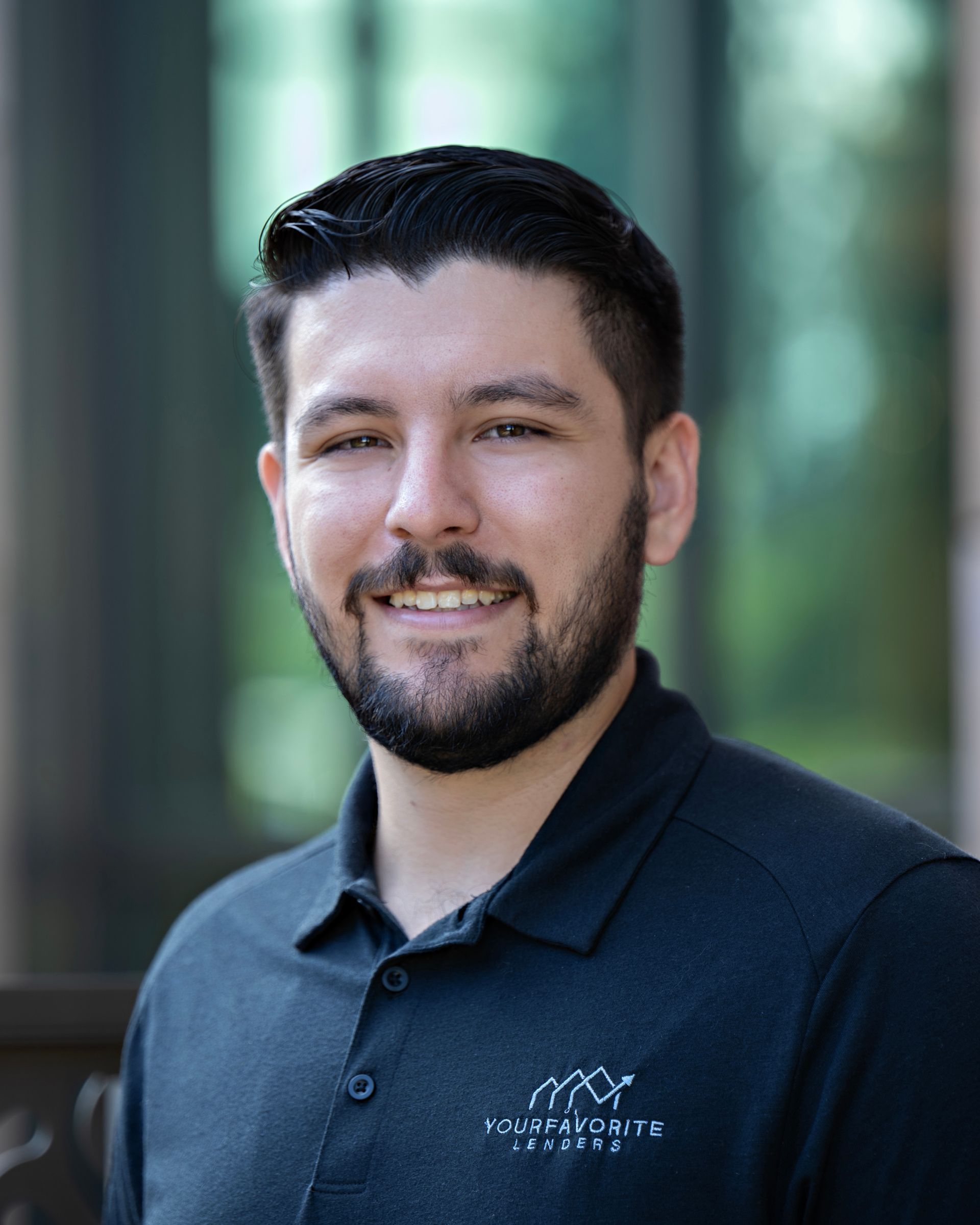 A man with a beard is wearing a black polo shirt and smiling for the camera.