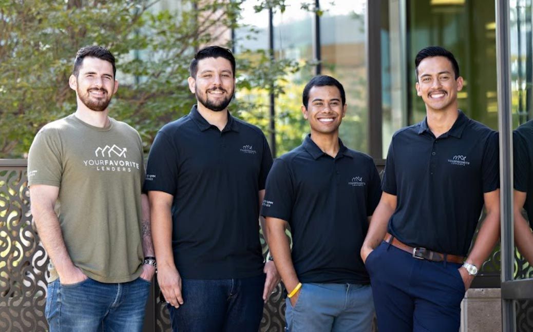 A group of four men are standing next to each other in front of a building.