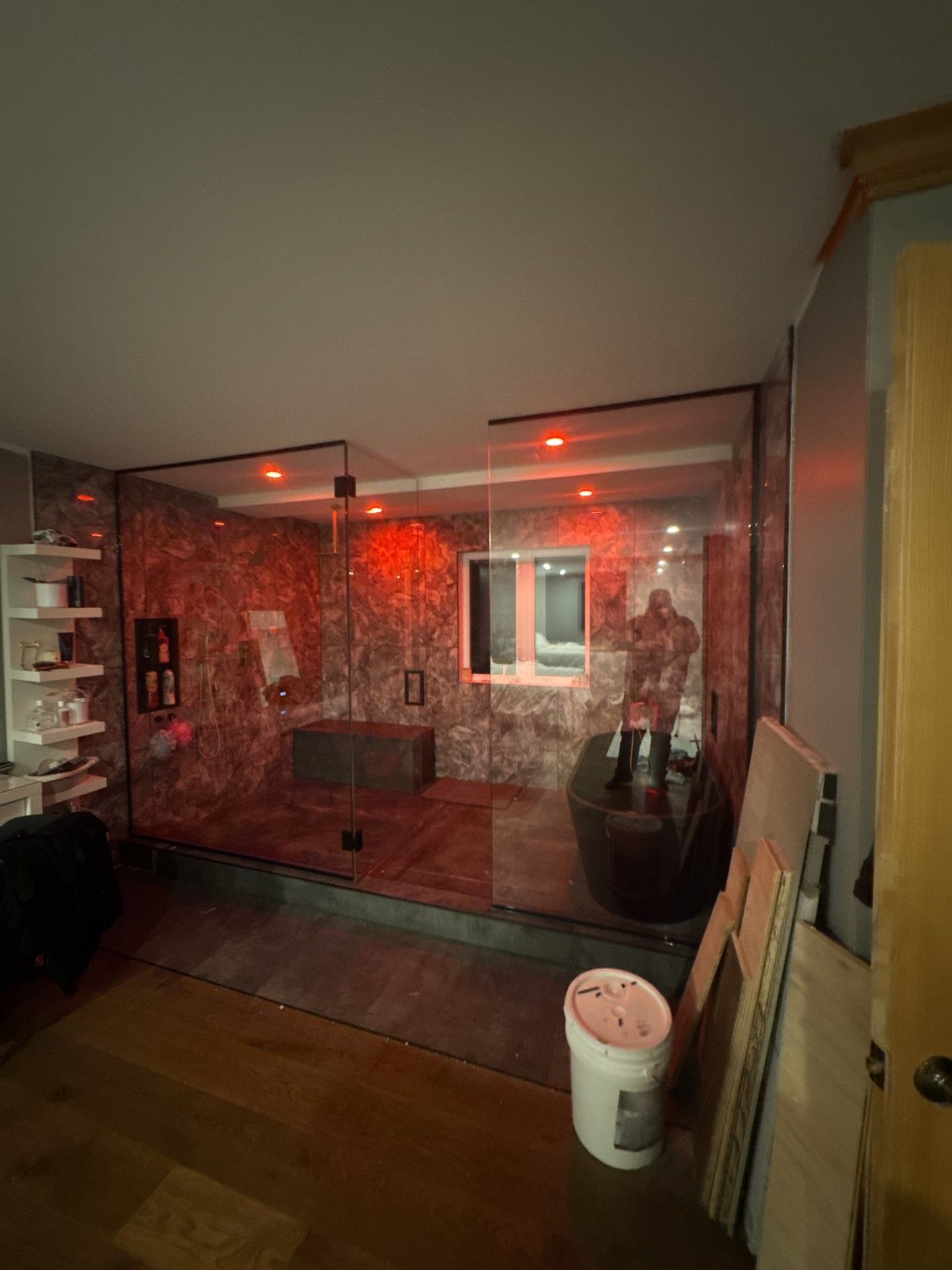 Salle de bains moderne avec cabine de douche en verre, éclairage rouge, baignoire îlot et carrelage en pierre foncée.