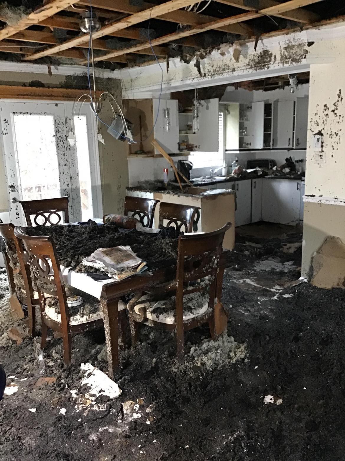 Vue intérieure d'une salle à manger et d'une cuisine endommagées par la fumée, avec des meubles et des plafonds carbonisés.