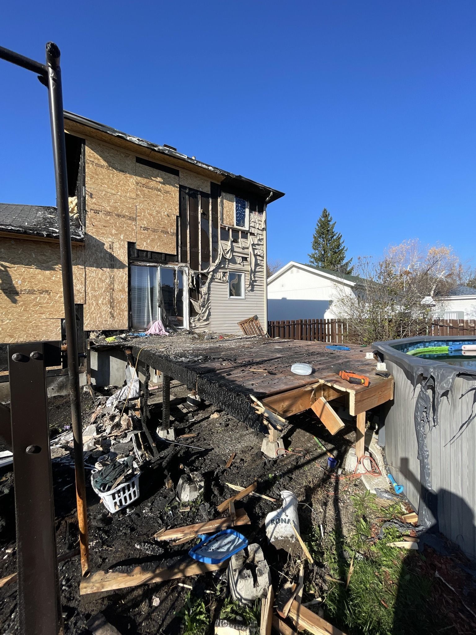 Vestiges calcinés d'une maison, terrasse effondrée, dégâts d'incendie visibles à l'extérieur. Ciel d'un bleu éclatant.