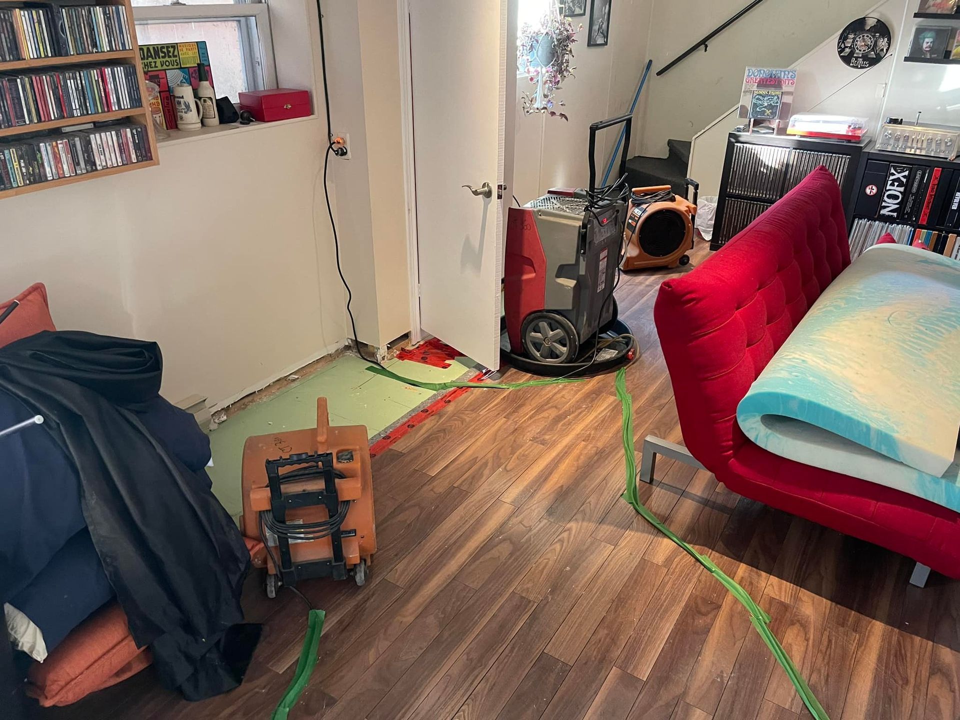 Salon avec parquet foncé, canapé en cuir noir, cheminée et petites fenêtres.