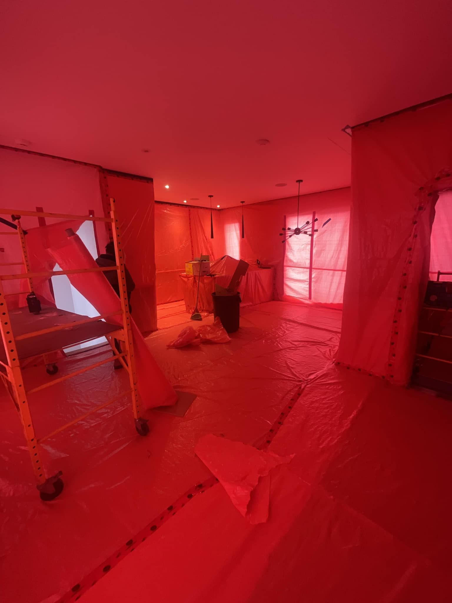 Pièce intérieure en travaux, recouverte de bâches en plastique rouge. Échafaudages visibles.