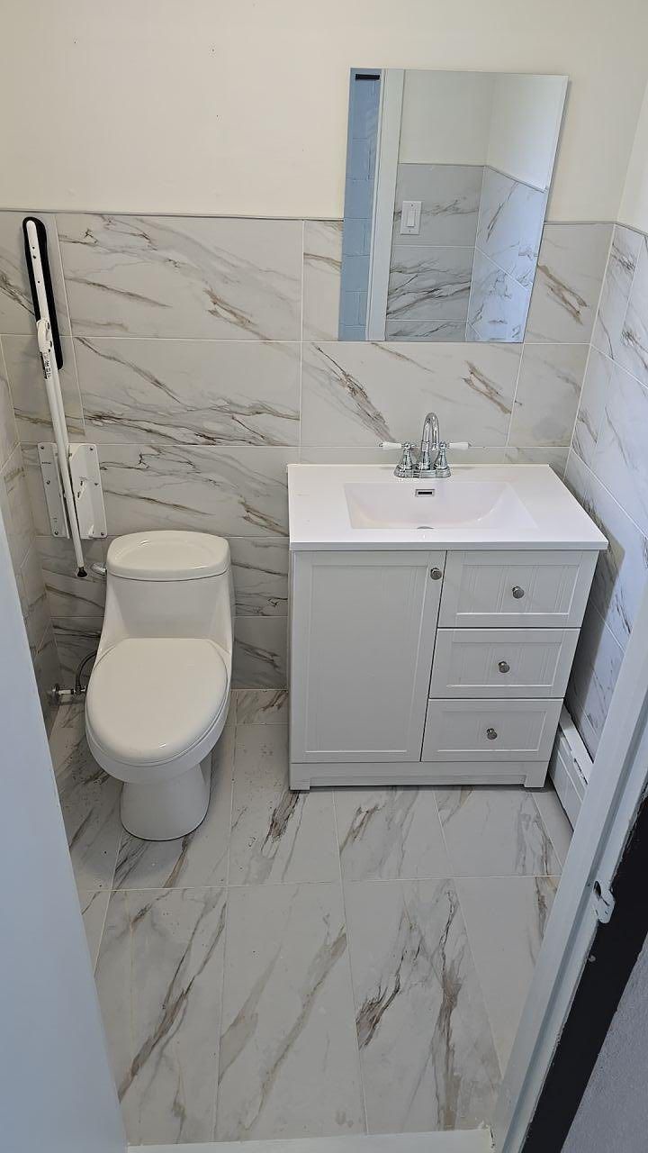 Petite salle de bains blanche avec carrelage imitation marbre, toilettes, meuble-lavabo, miroir.