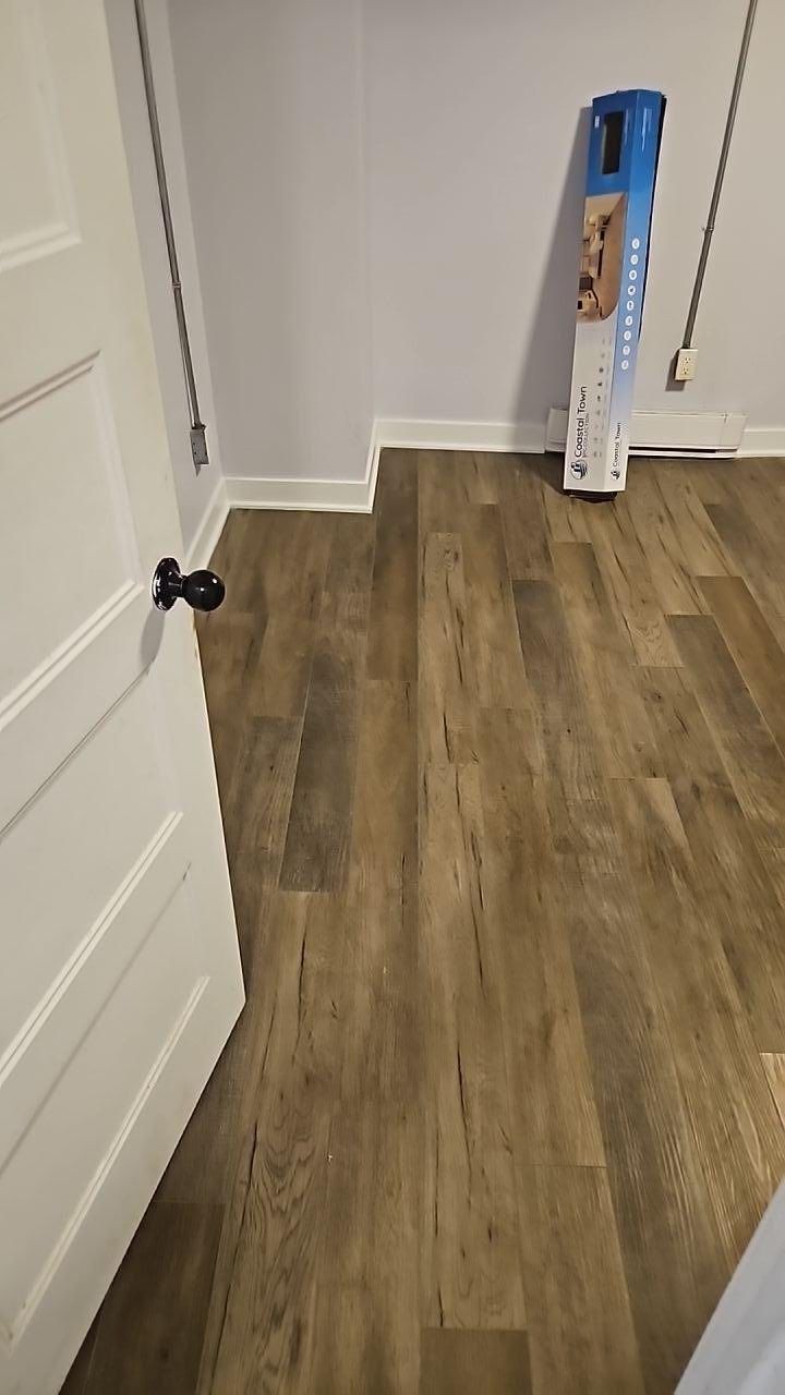 Porte entrouverte, nouveau revêtement de sol imitation bois et lames de parquet empilées contre un mur blanc.