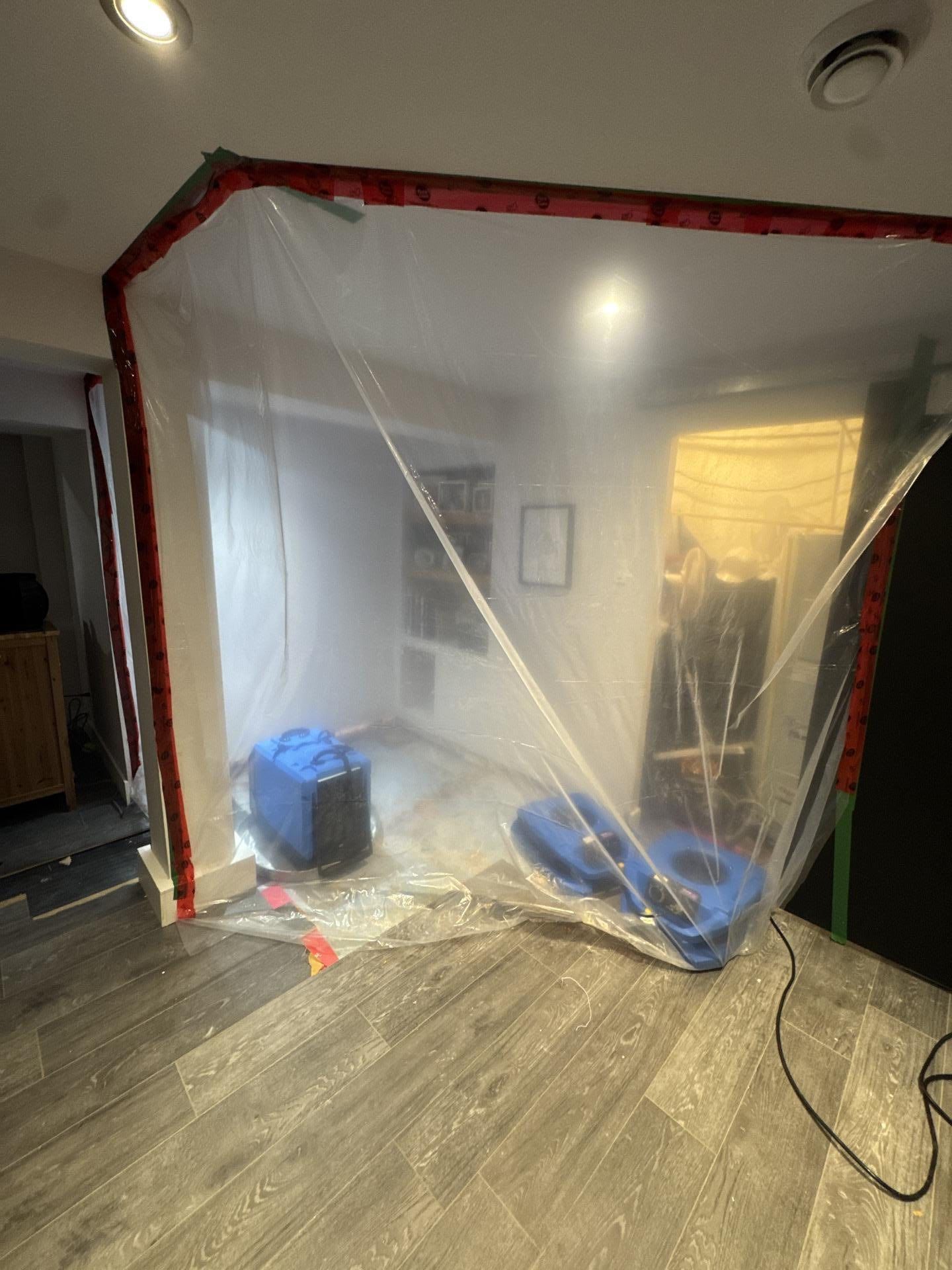 Une pièce recouverte de bâches en plastique, équipée de deux ventilateurs bleus pour éliminer l'humidité.