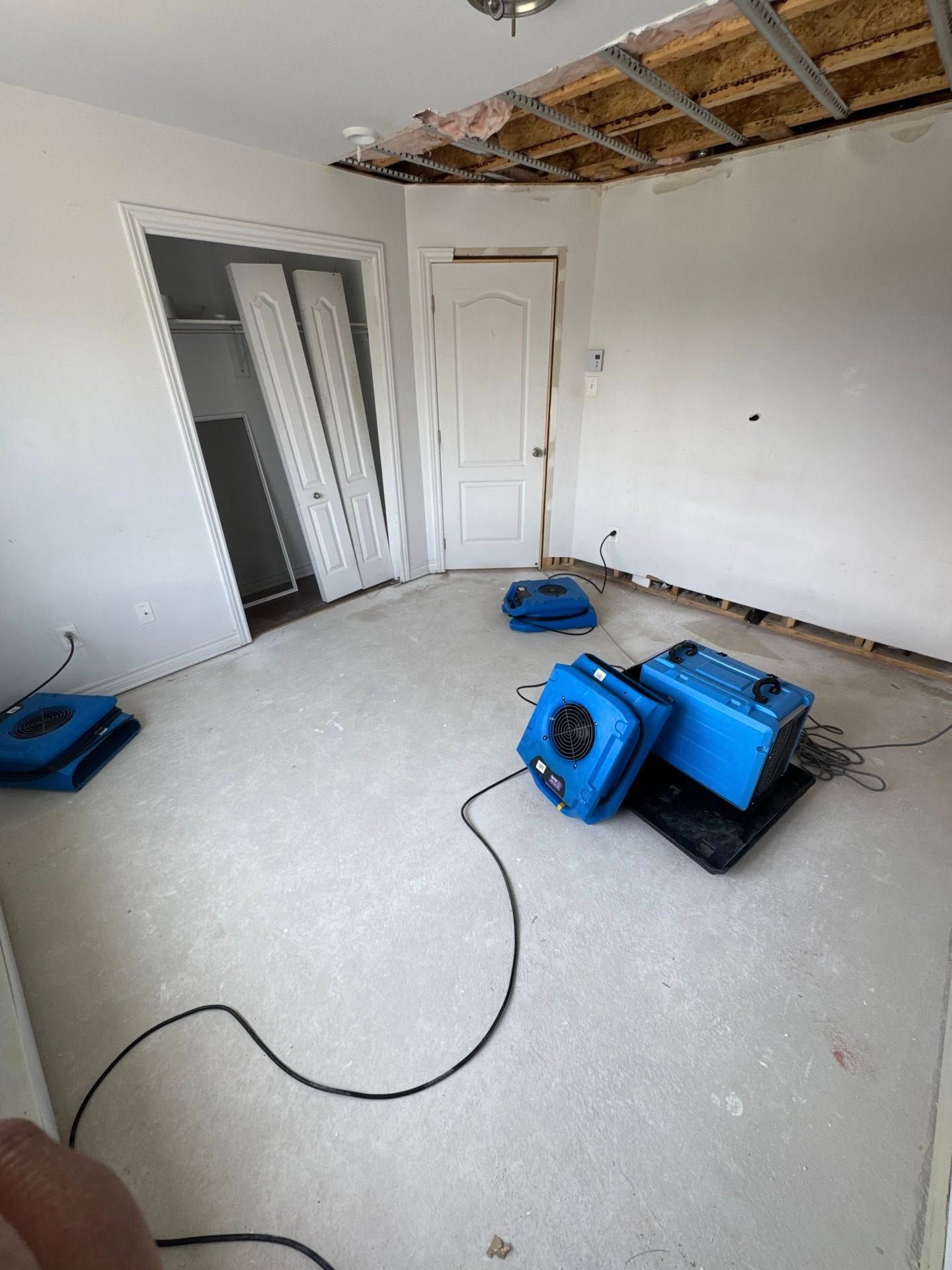 Pièce endommagée par l'eau : plafond apparent, ventilateurs de séchage au sol, porte du placard et encadrement de porte.