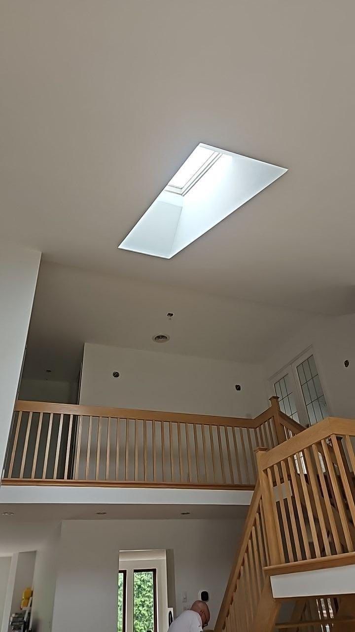 Vue intérieure d'une maison à deux étages avec puits de lumière. Rambardes en bois, escalier et murs aux tons neutres.