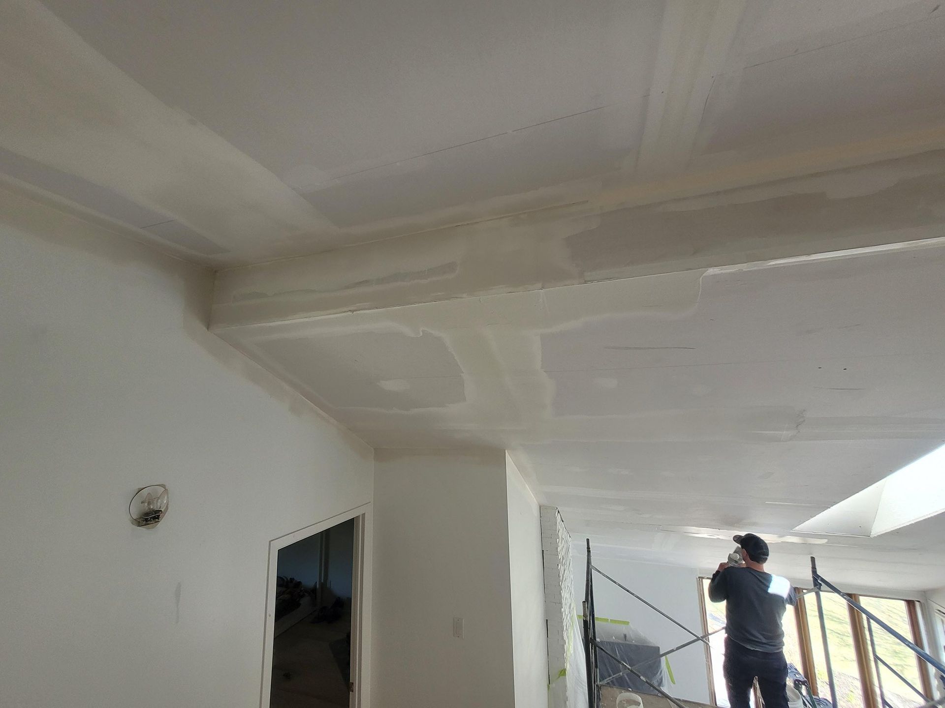 Homme travaillant sur un plafond en plaques de plâtre ; travaux de construction intérieure, murs blancs.