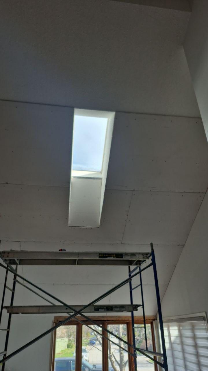 Vue intérieure d'une pièce avec un puits de lumière, des cloisons sèches et un échafaudage ; une fenêtre est visible en dessous.