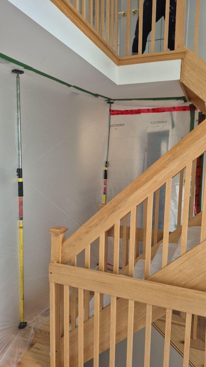 Escalier avec rampe en bois, protégé par une bâche en plastique et des poteaux pour travaux de construction ou de rénovation.