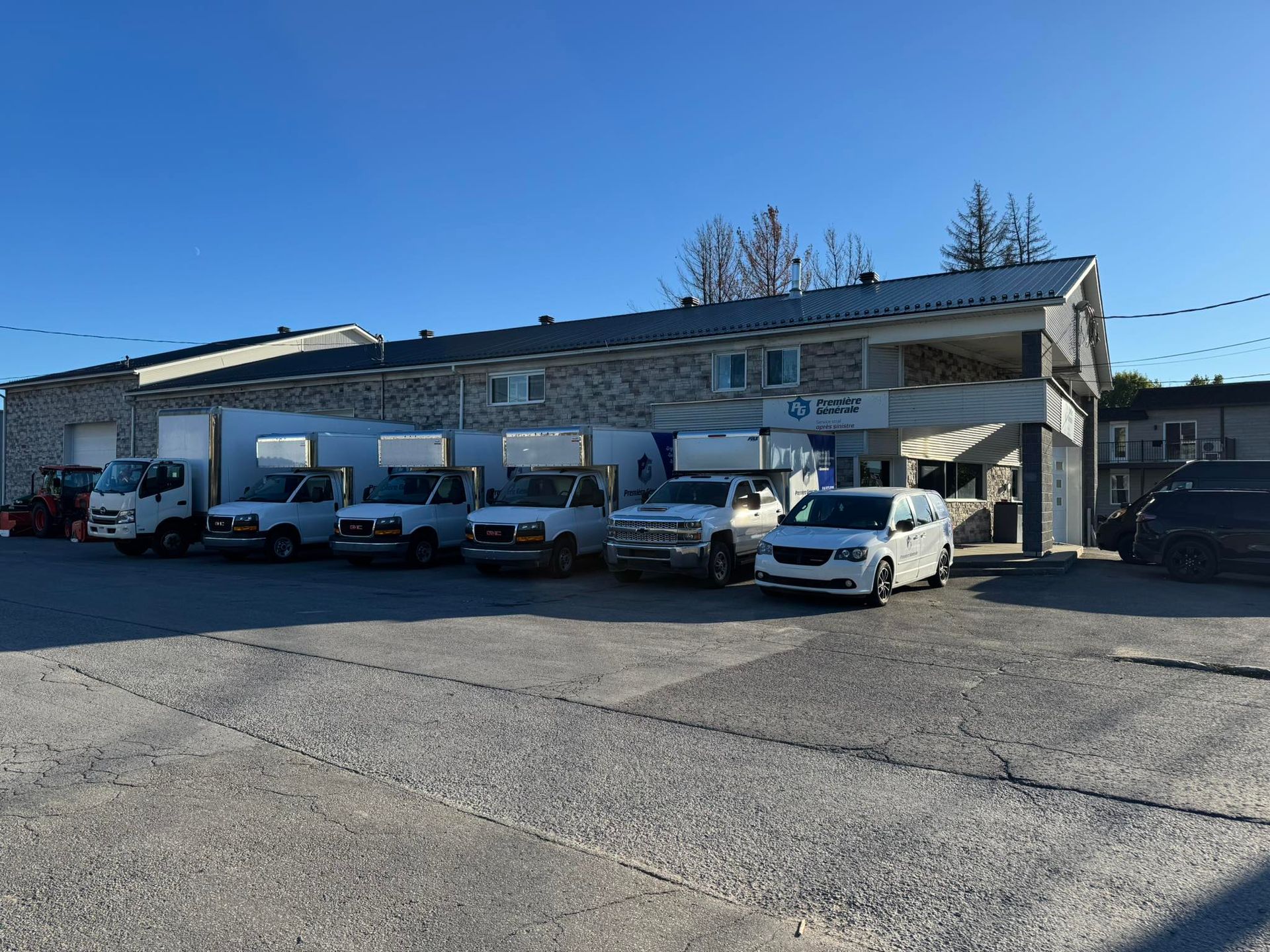 Véhicules stationnés devant un bâtiment en pierre portant l'enseigne « Pièces automobiles ». Journée ensoleillée.