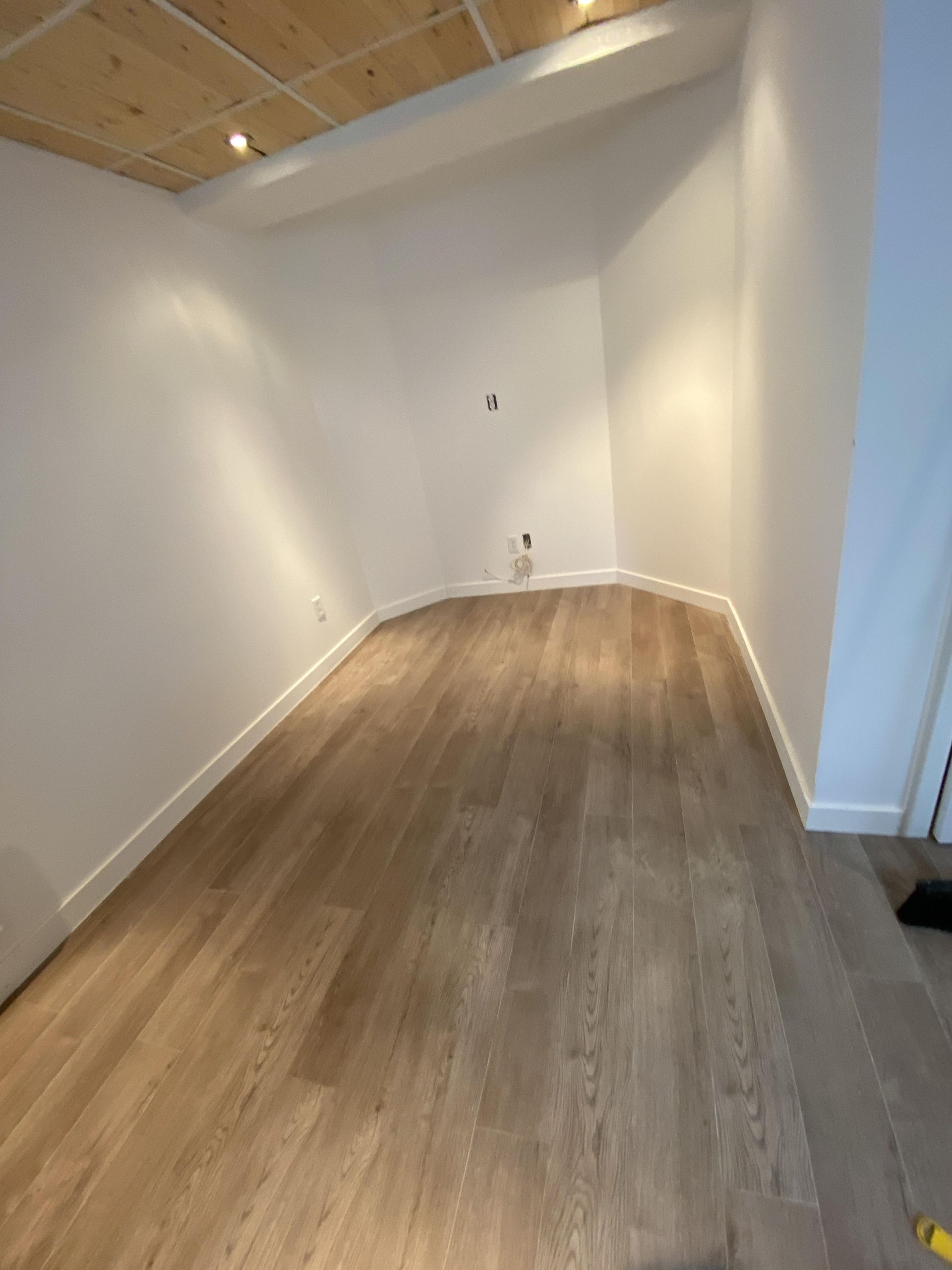 Pièce vide avec un mur incurvé et un parquet. Murs blancs, plafond en bois.