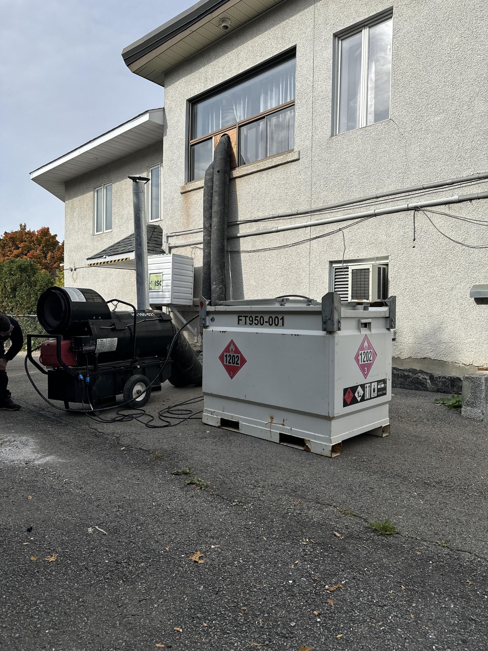 Bâtiment gris avec un système de chauffage et un conteneur à l'extérieur, reliés par un tuyau foncé.