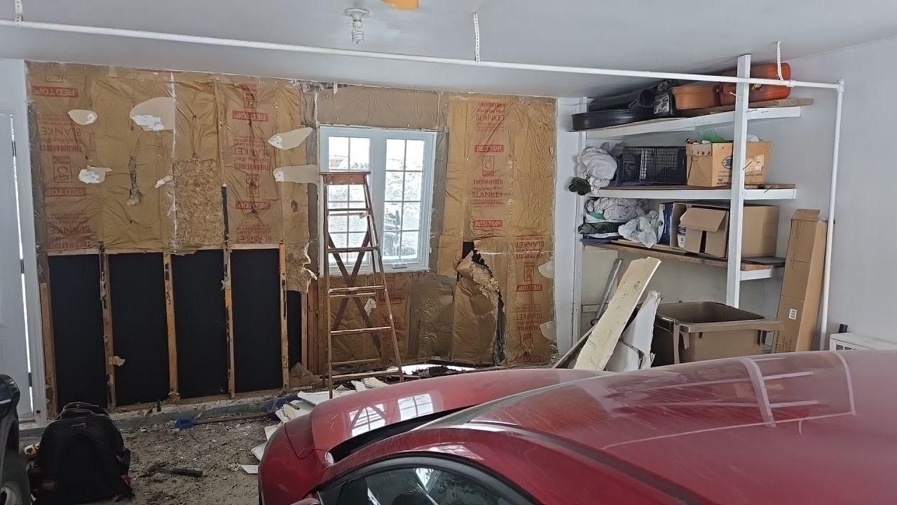 Intérieur du garage en mauvais état, avec isolation apparente, fenêtre, voiture rouge et étagère.